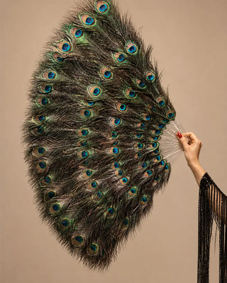 Adult cabaret model holding a large peacock feather fan at a side angle on a luxury black and gold stage