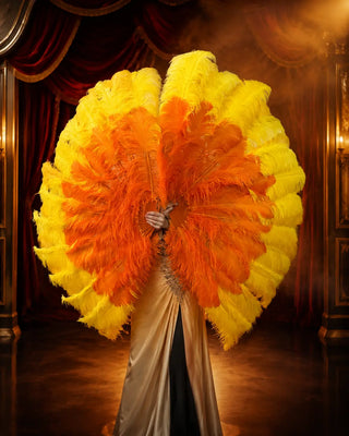 Yellow and orange three-layer ostrich feather fan pair arranged above and below a performer in a refined cabaret theater